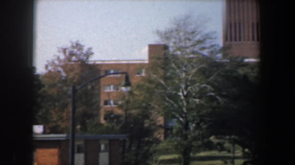 1960 Baltimore view of tan brick apartment buildings, trees, lawn, and a street lamp framed by dark foreground edges.