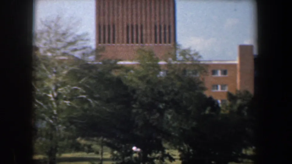 1960 Baltimore apartment exterior with a prominent slatted tower, tan brick walls, trees, and dark window-like foreground bars.