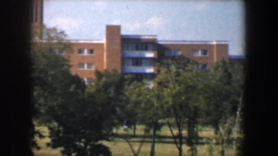 1960 Baltimore residential exterior showing tan brick apartments, balconies, trees, lawn, and dark foreground frame edges.