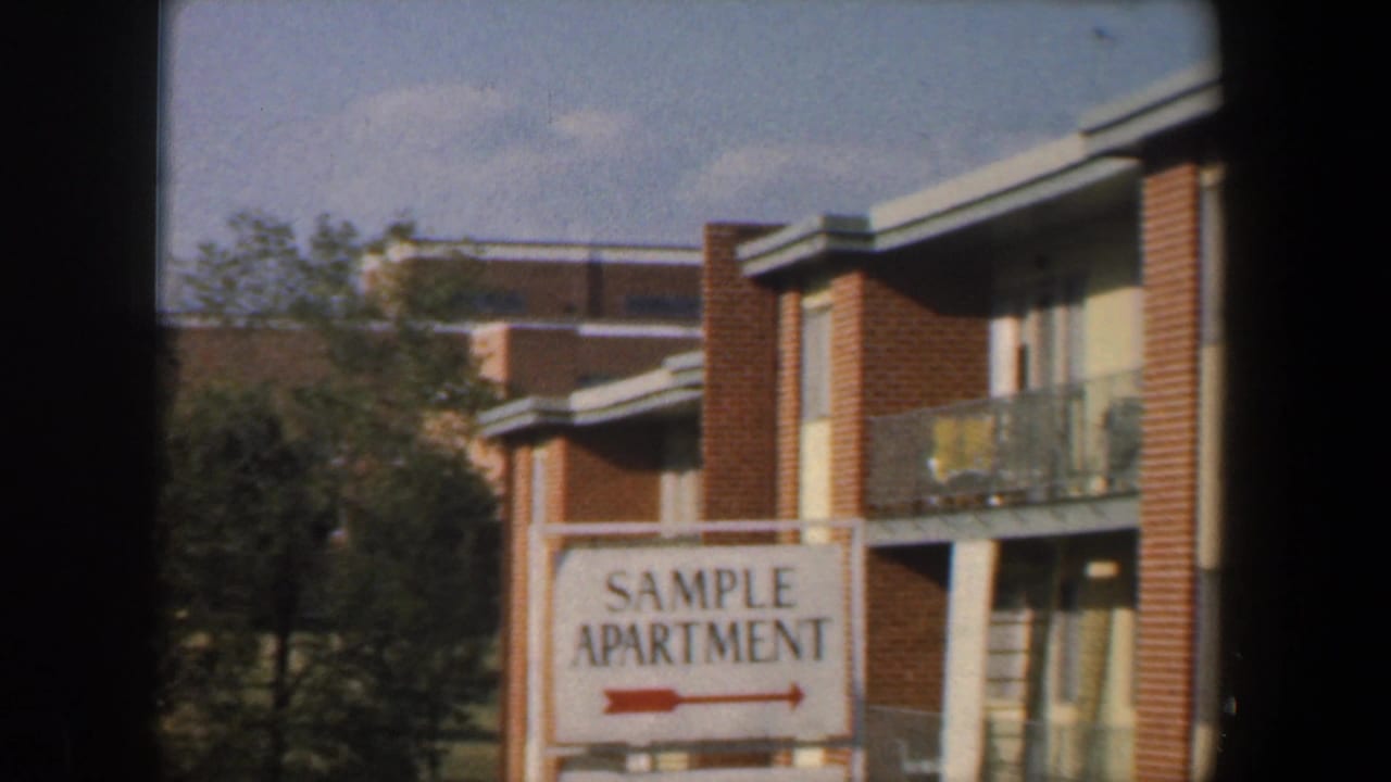 Brick apartment building seen through a window frame with a SAMPLE APARTMENT sign in front.