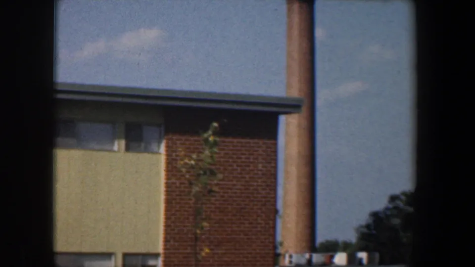 1960 Baltimore home-movie frame of an apartment building corner beside a utility pole, seen through window framing.