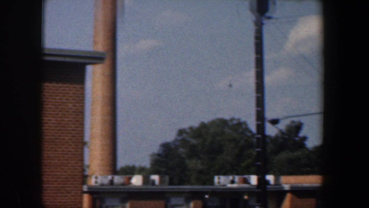 1960 Baltimore home-movie view of a brick apartment building, trees, utility pole, and dark window framing.