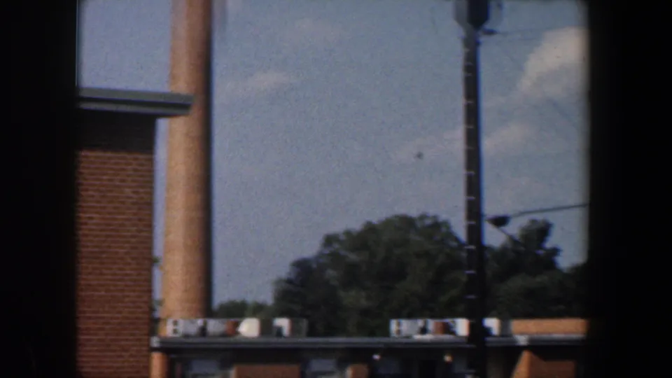 1960 Baltimore home-movie view of a brick apartment building, trees, utility pole, and dark window framing.