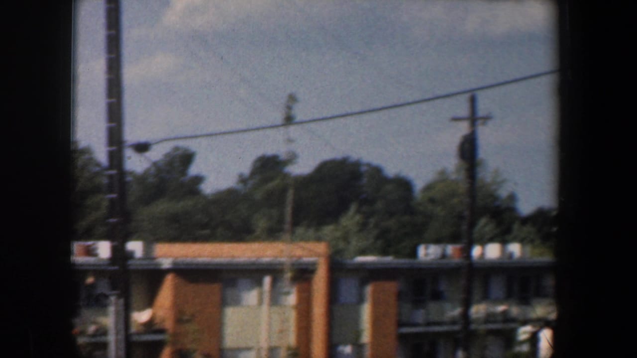 Low apartment buildings, utility poles, wires, trees, and a dark vertical window frame.