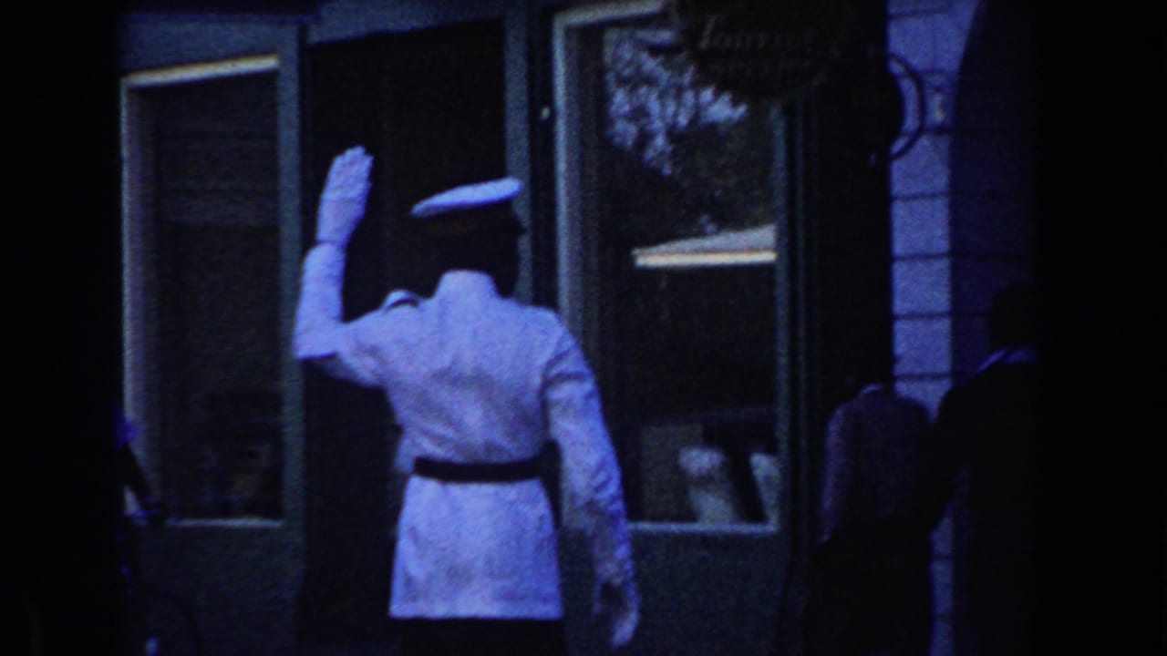 Traffic officer in a white uniform raises an arm beside storefront windows.