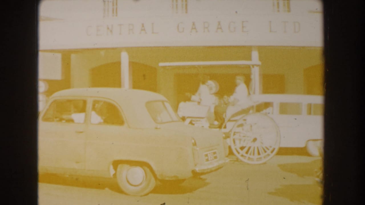 White car and horse-drawn carriage stand outside Central Garage Ltd with people nearby.