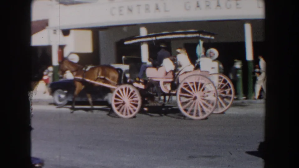 A side view shows a horse-drawn carriage with several riders moving across the frame near the Central Garage frontage in Nassau, Bahamas.