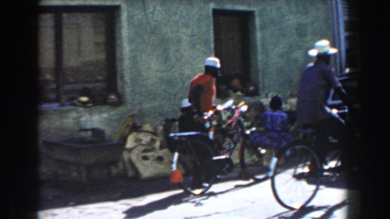 Cyclists and seated people outside a weathered street building.