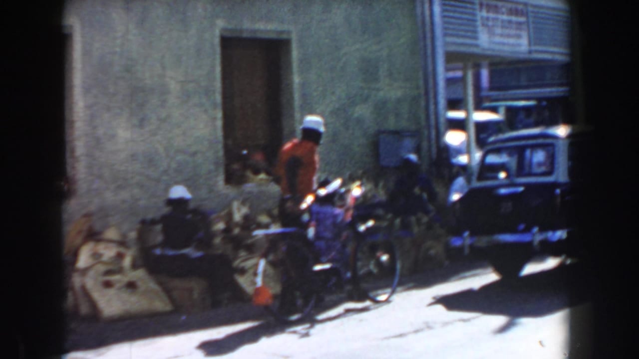 People and bicycles near a building with a parked dark car at right.