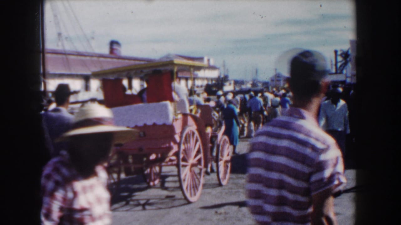 Red horse-drawn carriage on a busy street with pedestrians and low buildings.