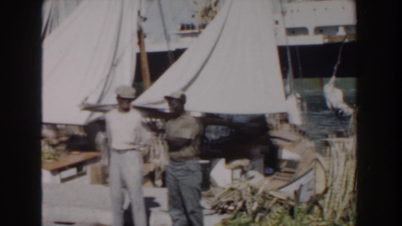 Men stand near white canvas tents and harbor gear beside sailboats.