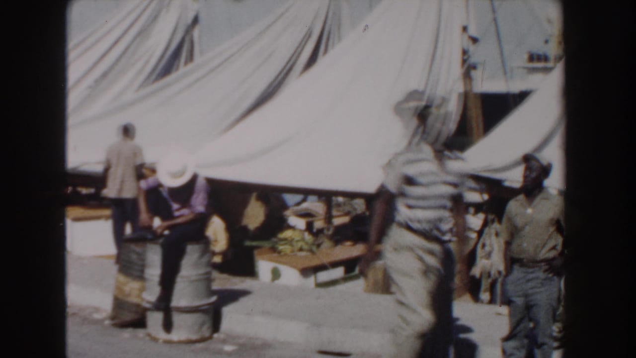 Workers stand and sit near barrels under white canvas tents.