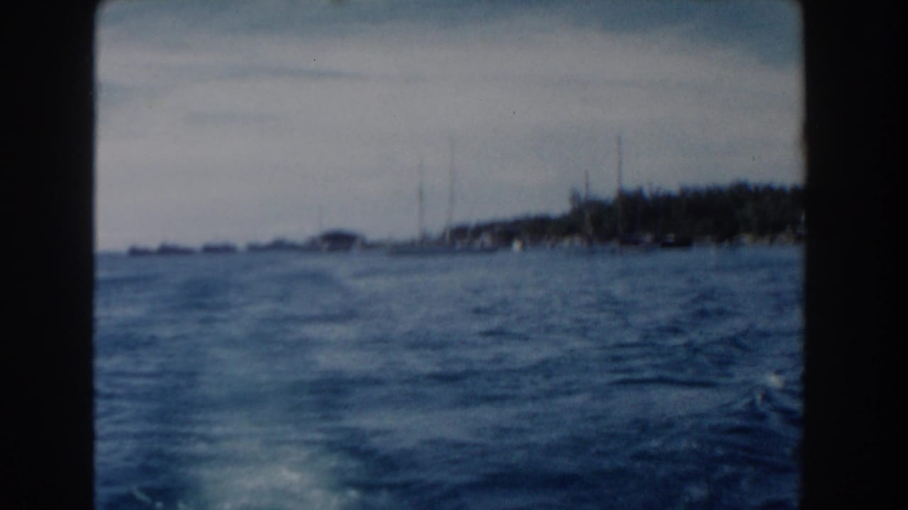 1961 Nassau harbor view from a moving vessel, showing blue water and a distant low shoreline through soft 8mm film.