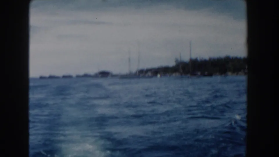 1961 Nassau harbor view from a moving vessel, showing blue water and a distant low shoreline through soft 8mm film.