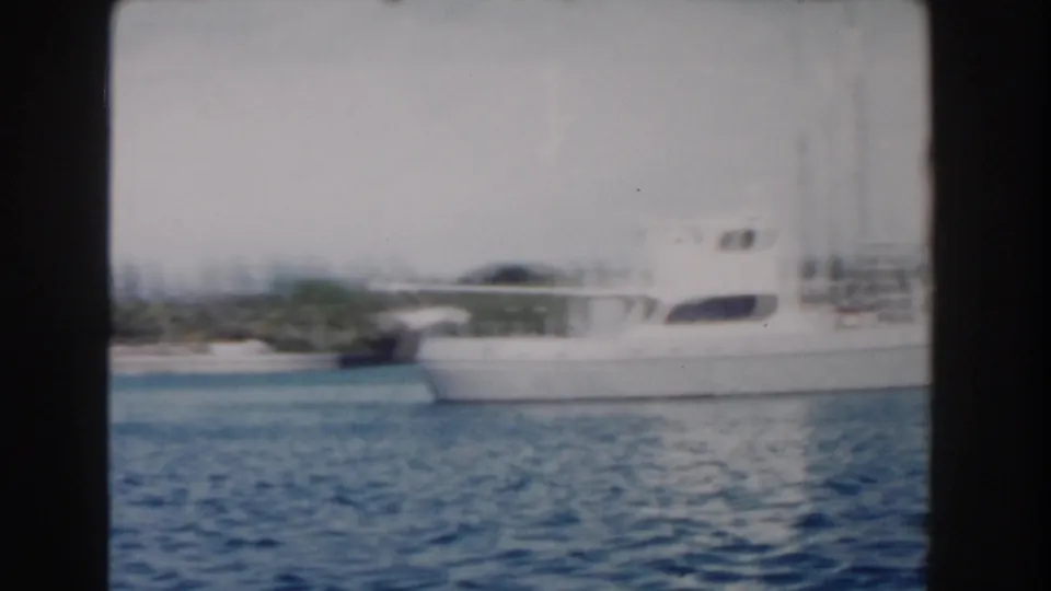 White motor yacht and shoreline seen from a moving vessel in 1961 Nassau harbor, with motion blur and soft 8mm exposure.