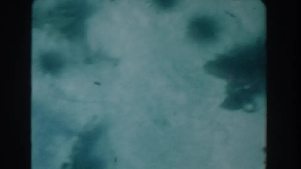 Soft blue-green 8mm frame, possibly water or an underwater view, with indistinct darker shapes and film specks.