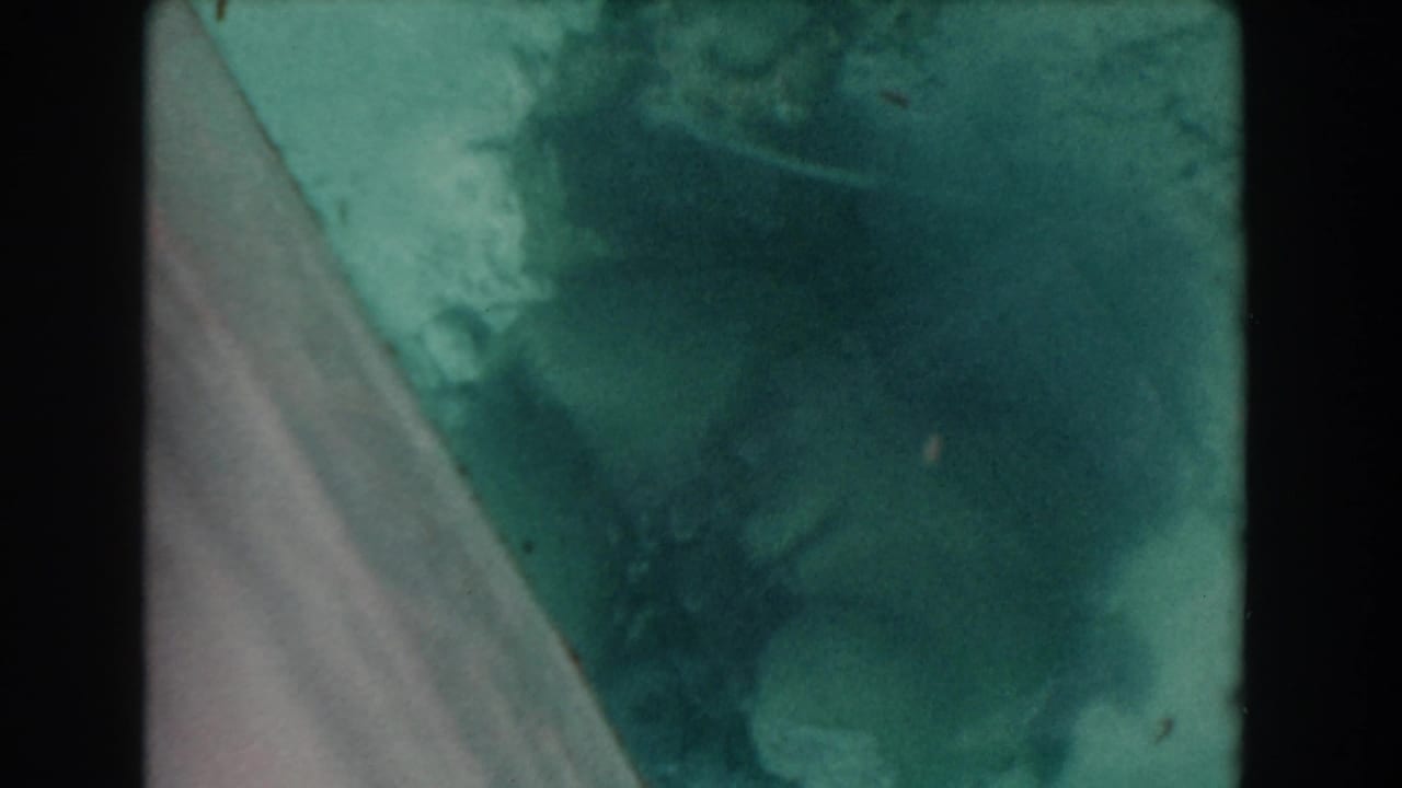 Green-blue water seen through glass with a diagonal frame edge and dark film borders.