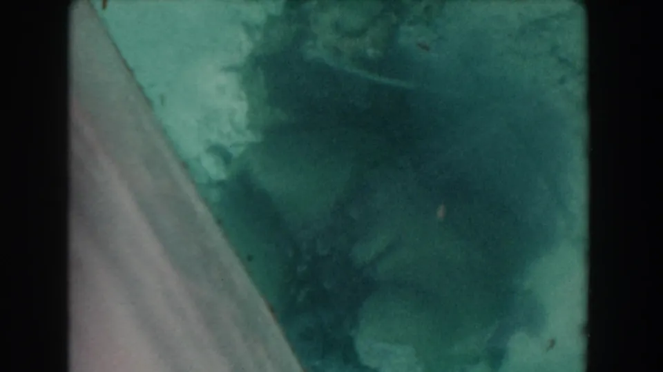 1961 Nassau 8mm frame showing murky green-blue water through glass, with a diagonal panel edge and soft film grain.
