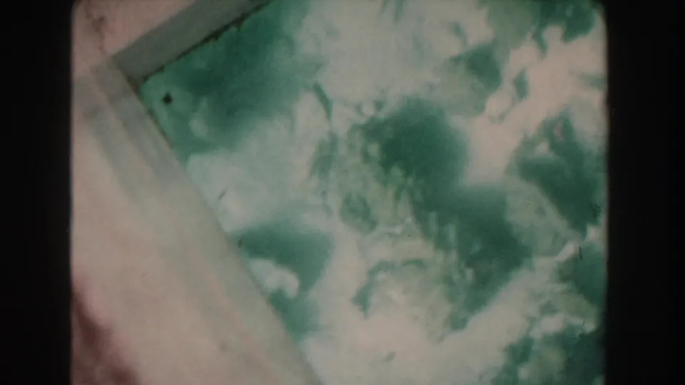 1961 Nassau 8mm frame of water viewed through glass, with pale frame edge, soft grain, and cloudy underwater detail.