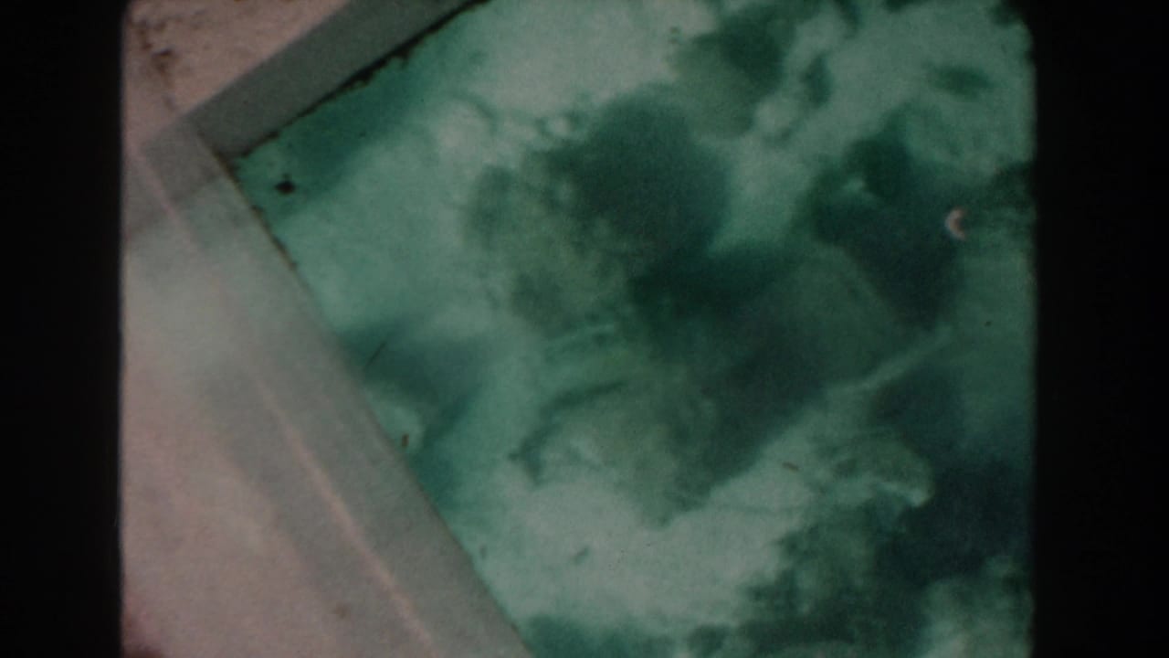 1961 Nassau glass-bottom boat view showing green water, indistinct coral texture, pale frame edges, and 8mm film grain.