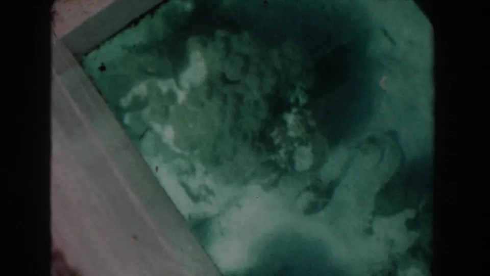 Green-tinted 1961 Nassau glass-bottom boat frame with indistinct coral, seabed texture, pale glass edge, and visible film wear.