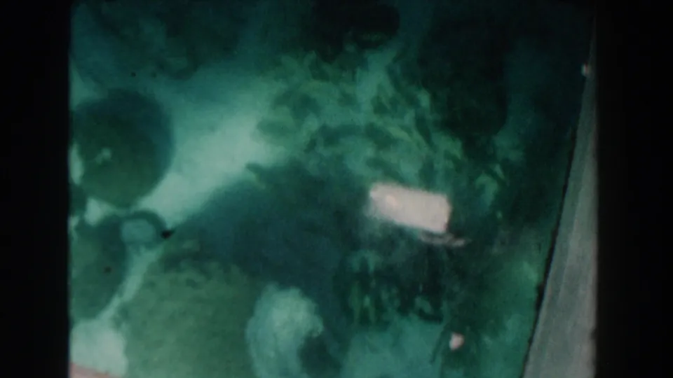 1961 Nassau boat-glass view showing murky seabed forms, possible coral or rock, green tint, and a bright reflected patch.