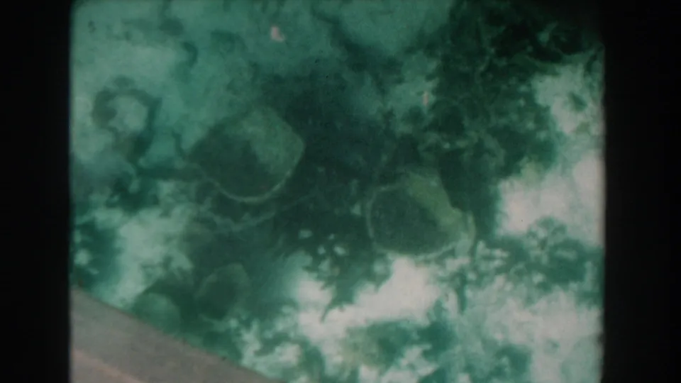 1961 Nassau 8mm underwater frame showing green water, pale seafloor, and indistinct coral or rock forms through a soft lens.