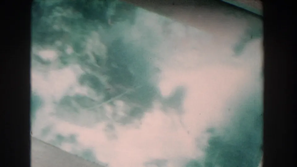 Soft 8mm underwater frame from Nassau showing a pale seabed area, shadowy reef forms, and murky green water.