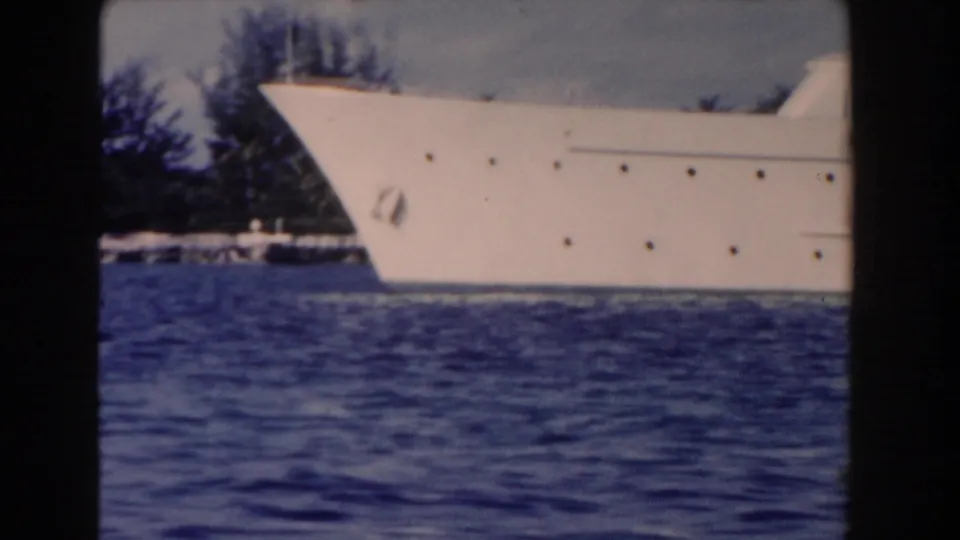 Large white yacht bow on blue water in the Nassau, Bahamas footage, with dark shoreline trees in the background.