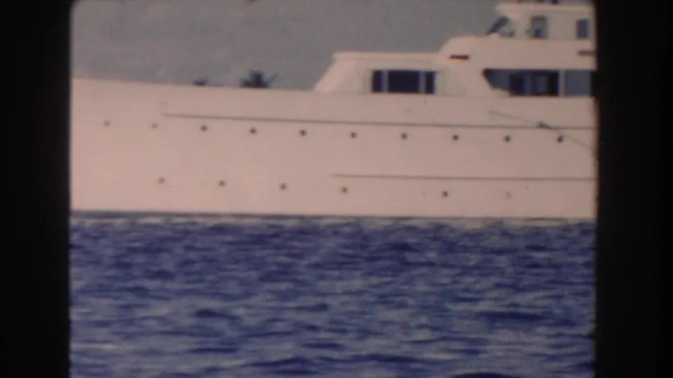 Side view of a large white motor yacht in Nassau, showing portholes, cabin windows, and blue water below the hull.
