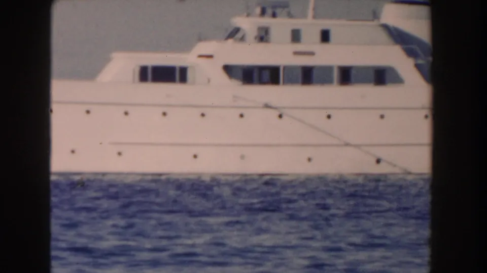 Midsection of the white yacht in the 1961 Nassau footage, with cabin windows, portholes, and rippled blue water in the foreground.