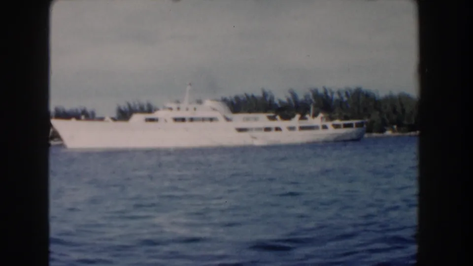 A wider 1961 Nassau harbor view shows the white cruise ship against dark shoreline vegetation and calm blue water.