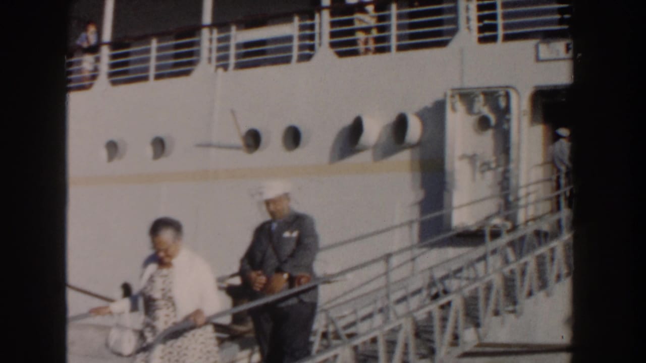 Adult passenger and uniformed crew member on a gangway beside the white ship.