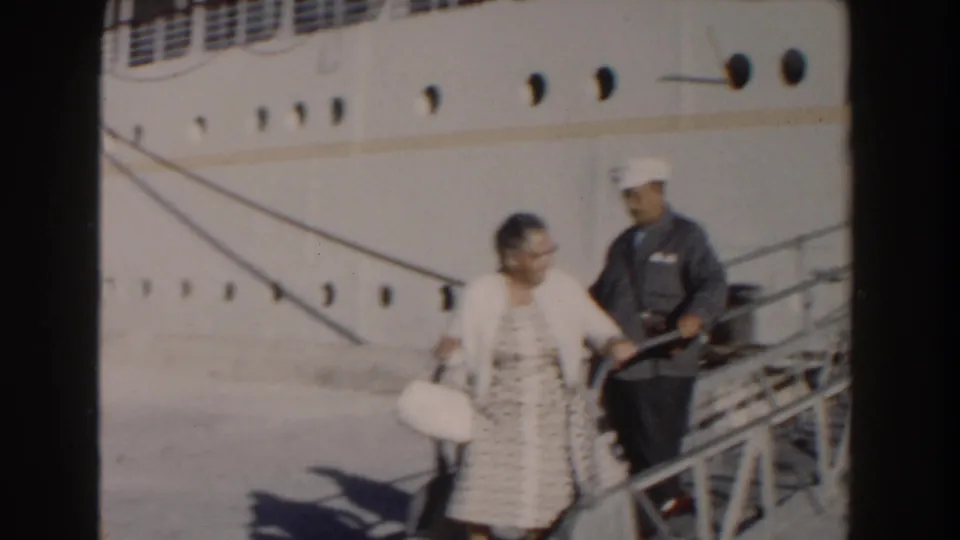 1961 Nassau home-movie frame showing an adult passenger and uniformed crew member on a sloped gangway beside the cruise ship.