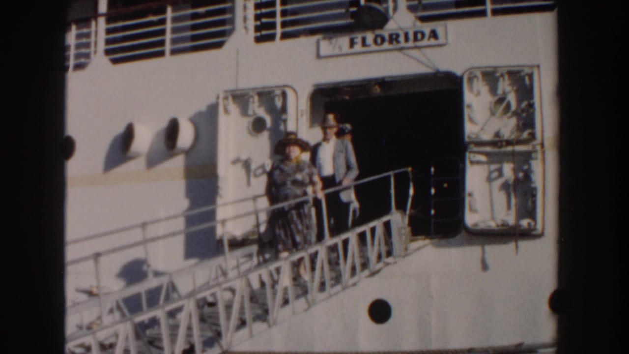 A man and woman stand on the gangway outside the ship doorway.