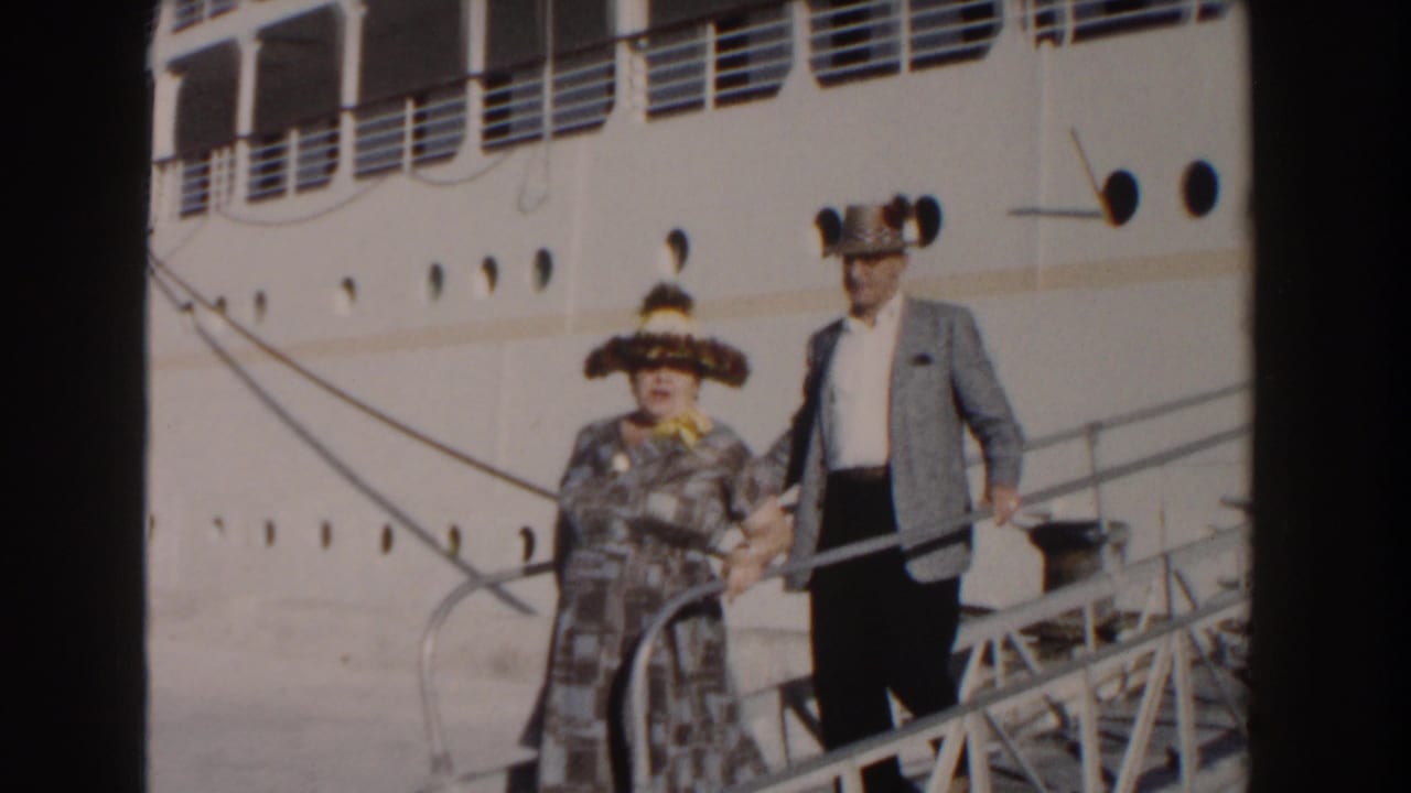 Elderly couple descending a cruise ship gangway beside a large white vessel.