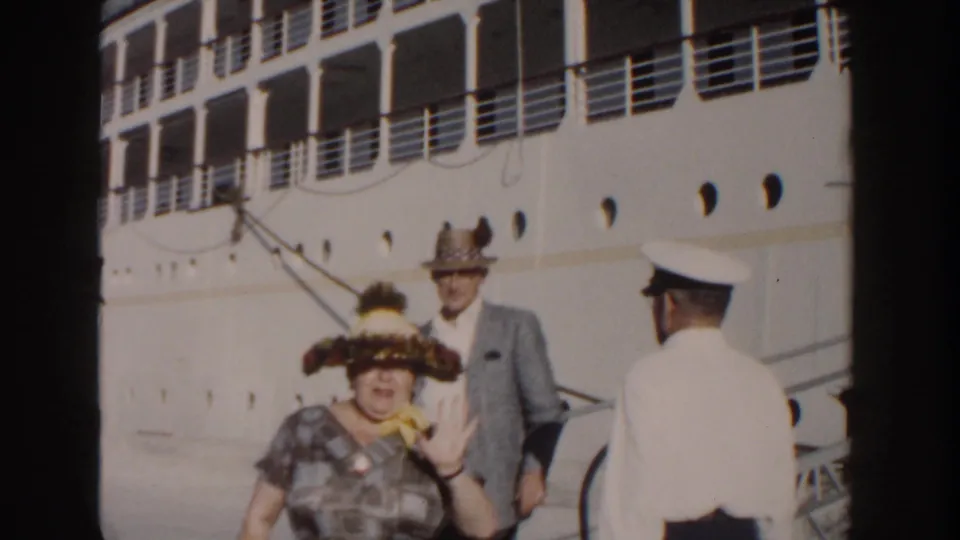 The woman appears to wave toward the camera as the couple reaches the lower gangway near a white-uniformed crew member in Nassau.
