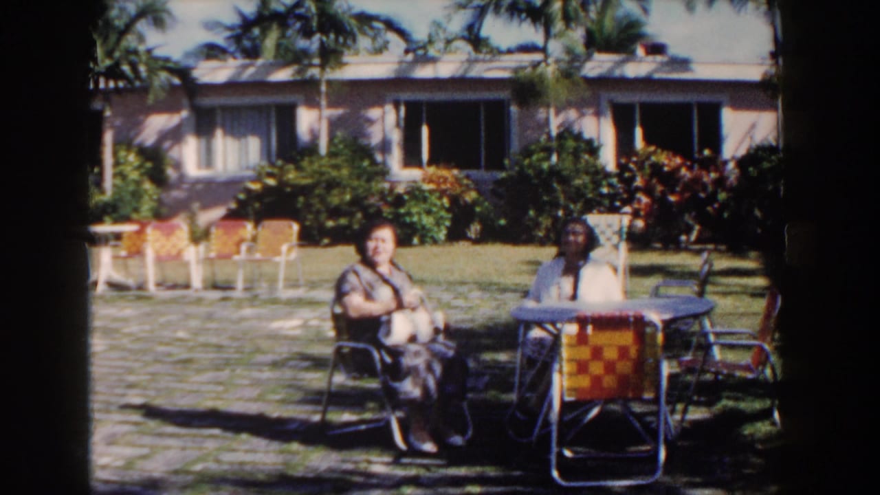 Two women sit at a round outdoor table with garden chairs nearby.