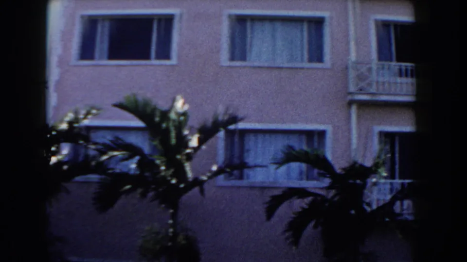 A pink stucco building with shuttered windows and balcony details appears behind palm fronds in the Nassau home-movie footage.