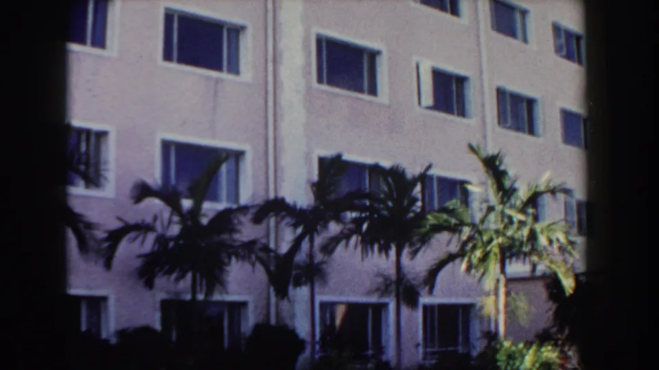 1961 Nassau frame showing a pale building side with repeated rectangular windows, palm trees, and bright tropical light.