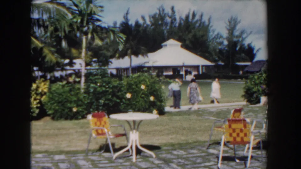 Nassau resort garden scene with three adults on a sidewalk behind colorful patio chairs and a white-roofed building.