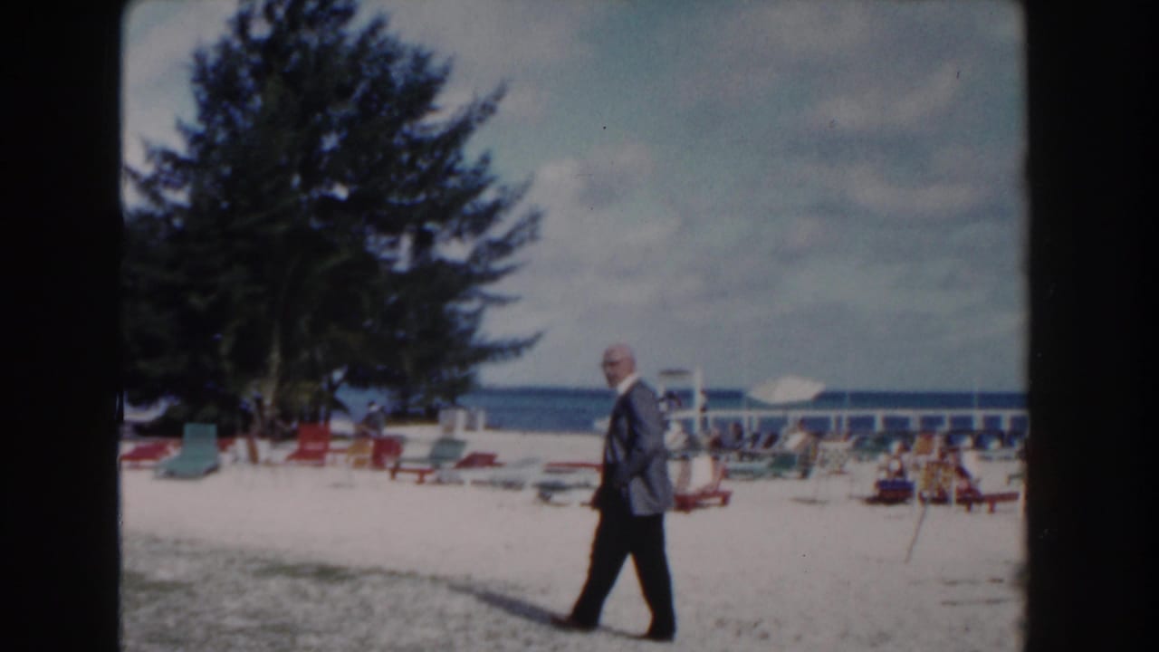 Man walks near beach chairs with a large tree and blue ocean in the background.
