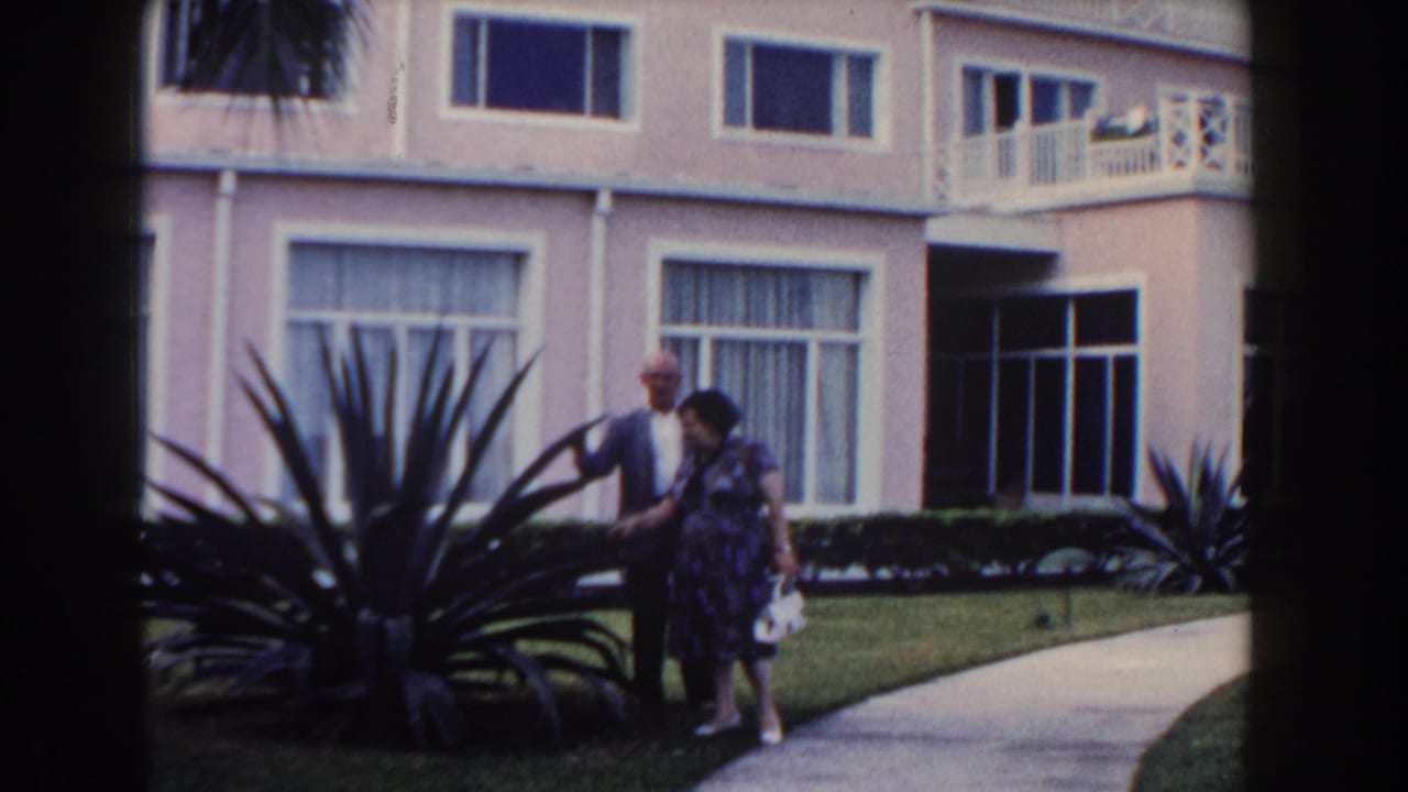 1961 Nassau home-movie frame showing a couple near agave-like landscaping outside a pink resort-style building.