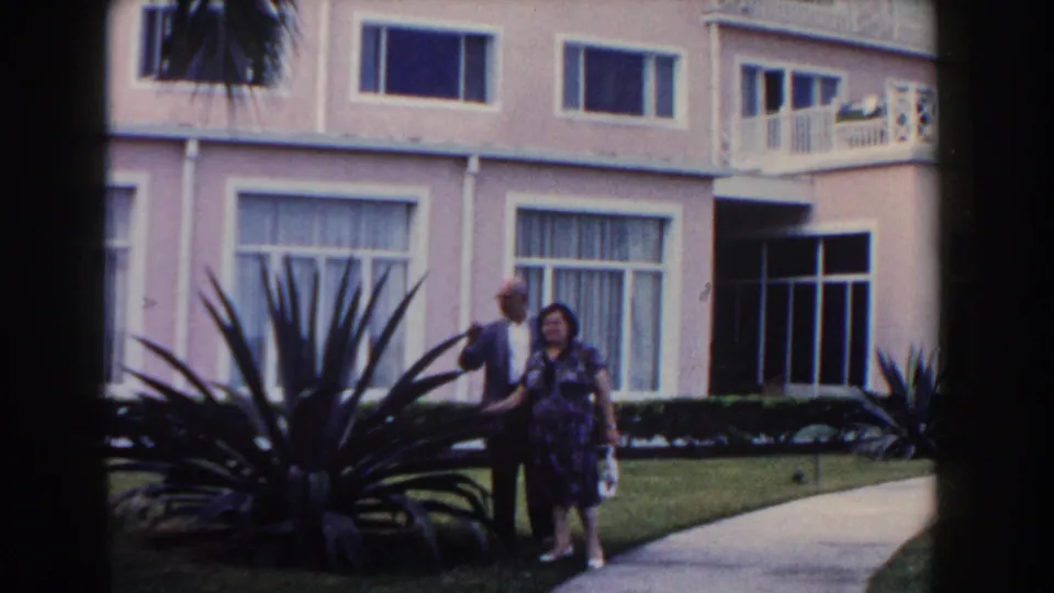 1961 Nassau footage shows a couple strolling along a garden path in front of a pink resort building.