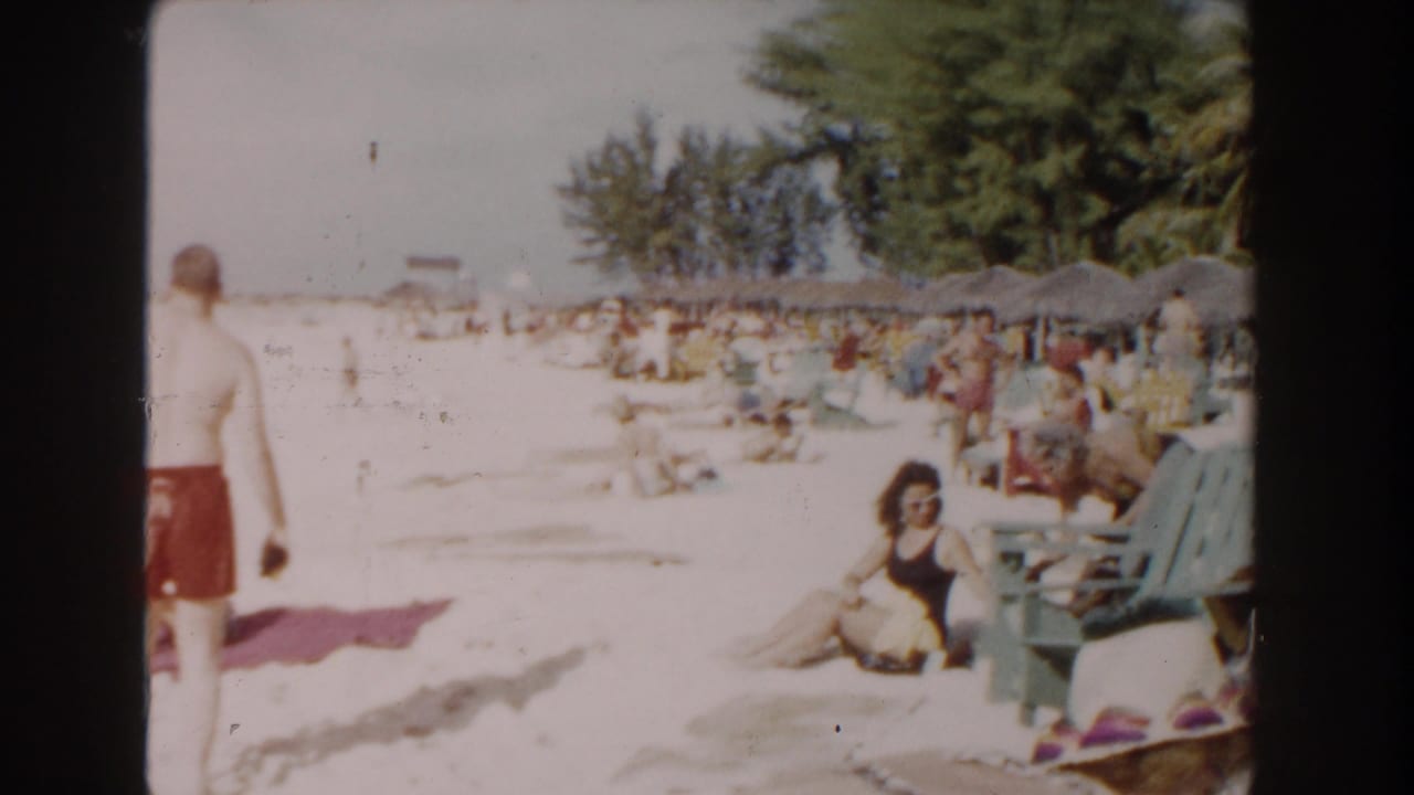 Beachgoers relax on bright sand near colorful chairs and thatched umbrellas.