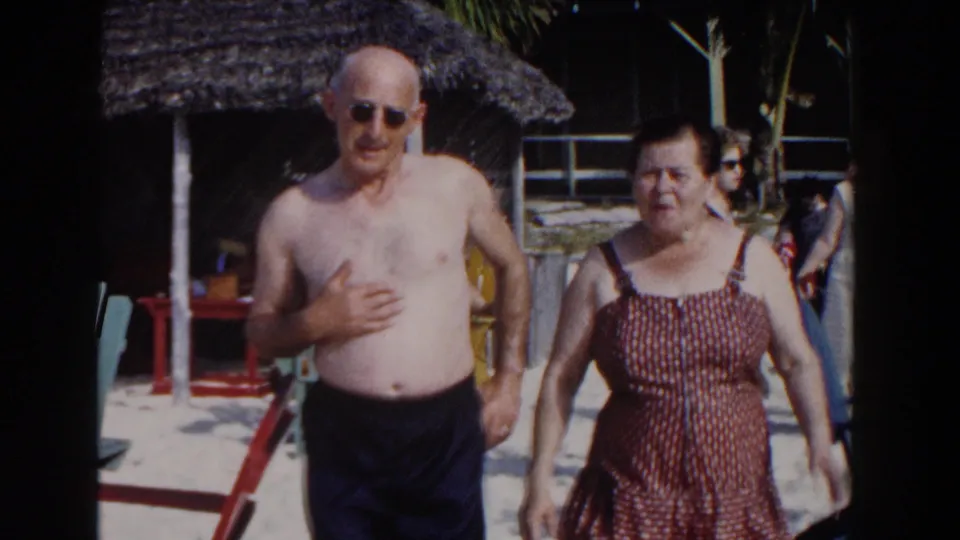 Near the end of the Nassau beach shot, the couple fills the frame as other vacationers and resort seating remain visible behind them.