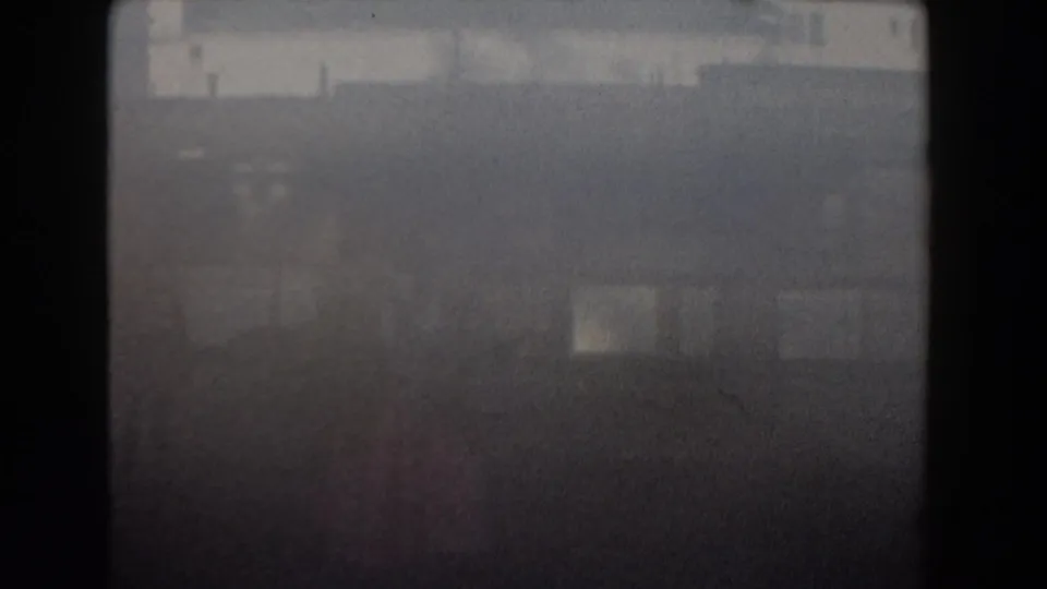 A mostly dark and blurred 8mm frame shows faint resort shapes, likely from an exposure shift or transition within the home-movie clip.