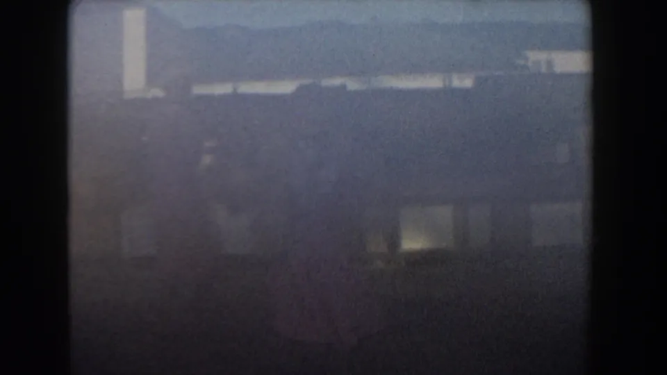 Hazy 1961 Nassau frame with pale structures, dark film border, and indistinct movement where the woman appears.