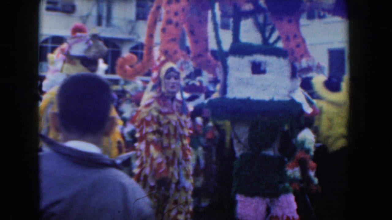 Masked and costumed parade participants move near a large decorated structure.
