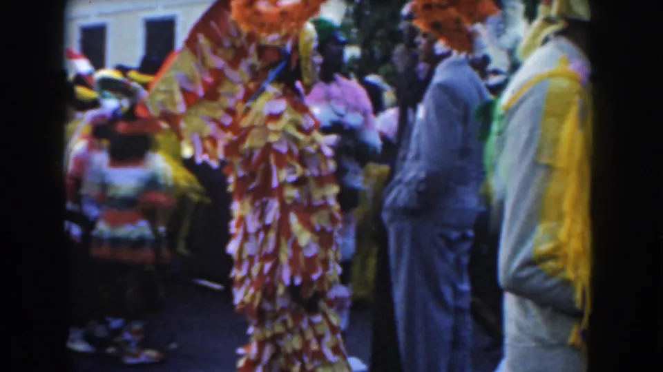 1961 Nassau parade scene shows a ruffled costume performer amid spectators and other colorful marchers.